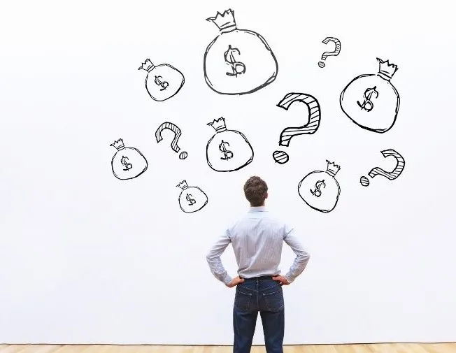 Man in a white shirt and pants facing a wall that is covered in drawings of money bags with question marks on them