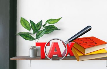 Shelf with books and glasses and the word tax under a magnifying glass