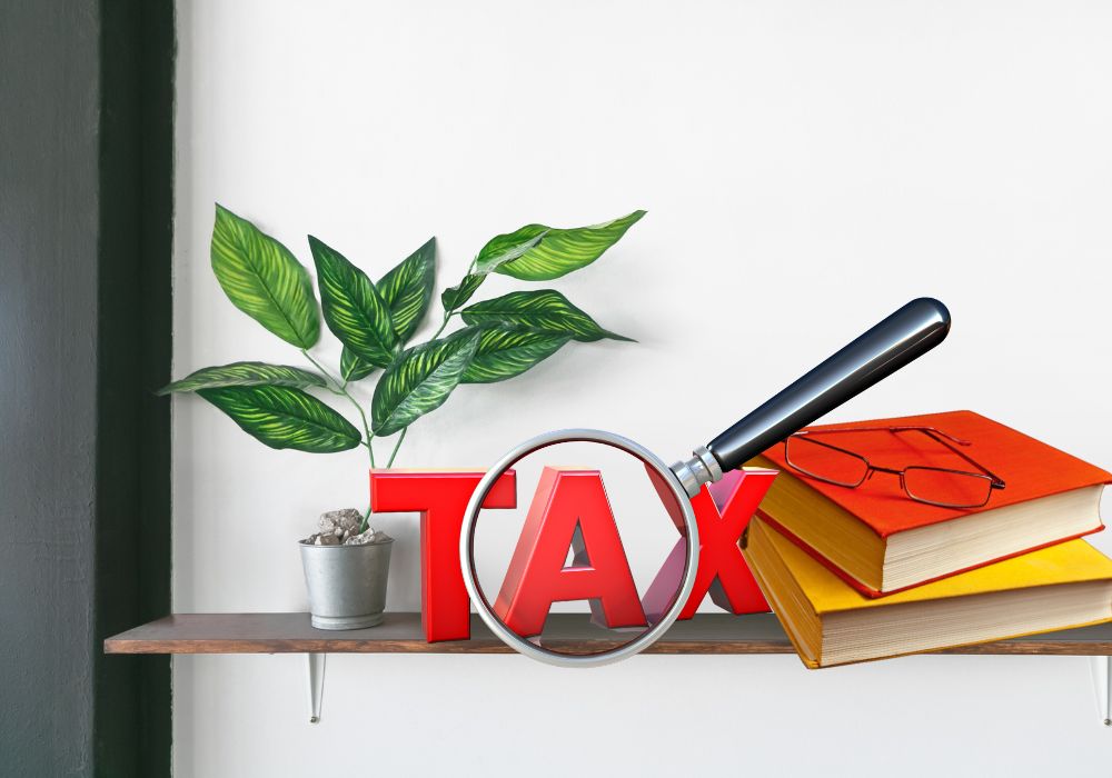 Shelf with books and glasses and the word tax under a magnifying glass