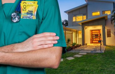 A doctor in green scrubs standing out the front of a modern australian home with $50 notes in his pocket and a stethoscope around his neck.