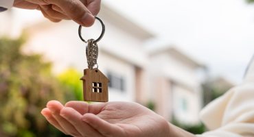 Woman being handed a key chain shaped like a house in front of a new built property with a house