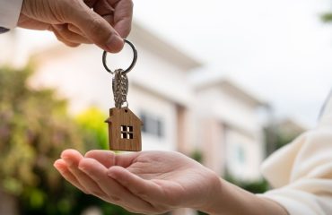 Woman being handed a key chain shaped like a house in front of a new built property with a house