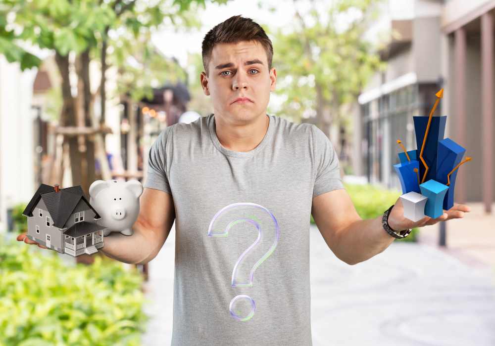 Man in a grey t-shirt showing confusion about a house and savings decision in one hand and an investment opportunity in the other. Standing in a leafy green street.