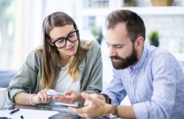 A man with a beard and a women with glasses in their home office discussing finances