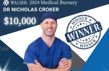 Doctor standing in front of a sign that announces he has won a $10,000 medical bursary.