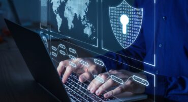 Man in blue button up shirt typing on a laptop computer with graphics of cyber security signs and a world map.