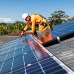 Man in a hard hat, orange workwear and harness, installing solar panels to a house roof in Brisbane