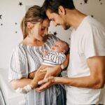 Young male and female couple cradle their newborn baby in the nursery of their home