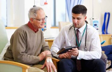 Young doctor speaking to a doctor in his late 60's about a treatment over an ipad.