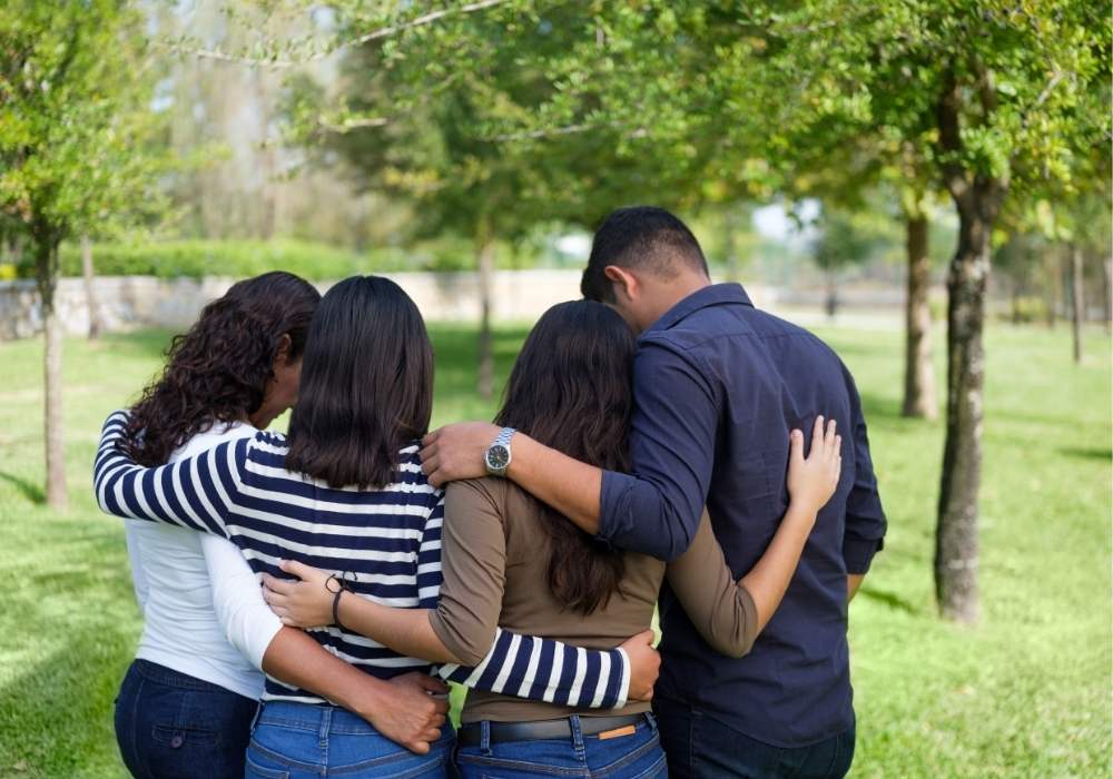 A family in grief huddle together in a beautiful green park.